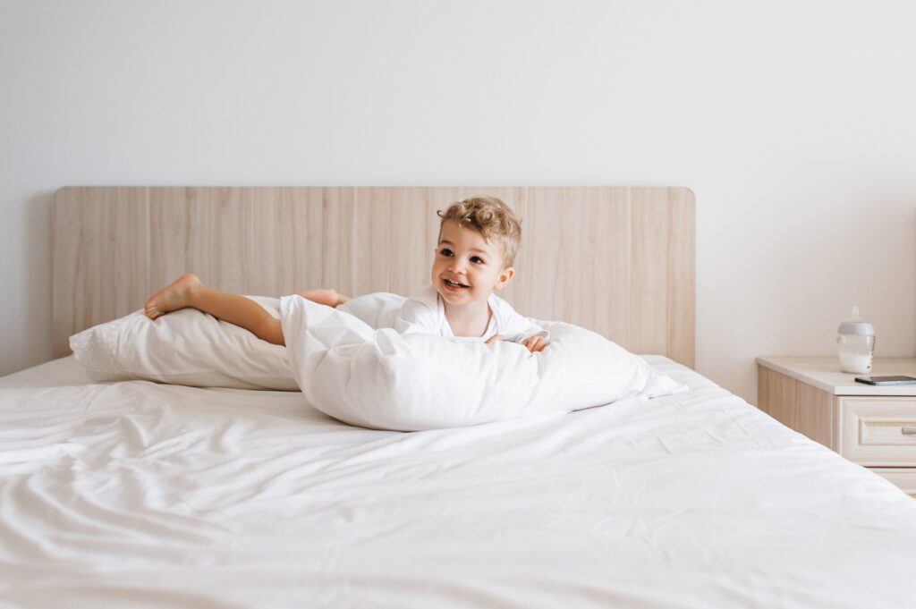 smiling toddler boy in white bodysuit lying on pil 2022 12 16 18 41 24 utc